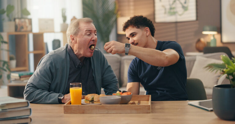 Home, caregiver and feed senior man in retirement for nutrition, assistance and lunch meal. Assisted living, nurse and helping old person with eating in lounge for rehabilitation and homecare service.