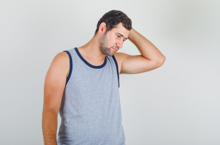 Young man looking down while holding head in grey singlet and looking exhausted , front view.