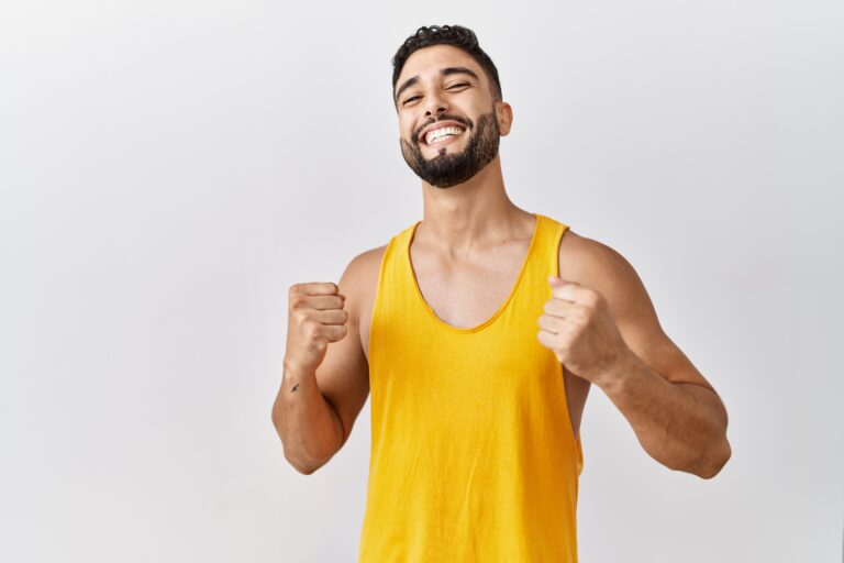 Young handsome man with beard standing over isolated background very happy and excited doing winner gesture with arms raised, smiling and screaming for success. celebration concept.